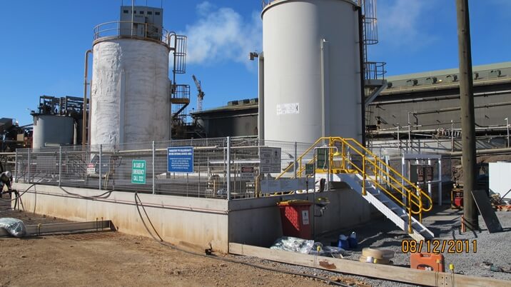 Two large tanks in front of a factory equipped with belt conveyors.
