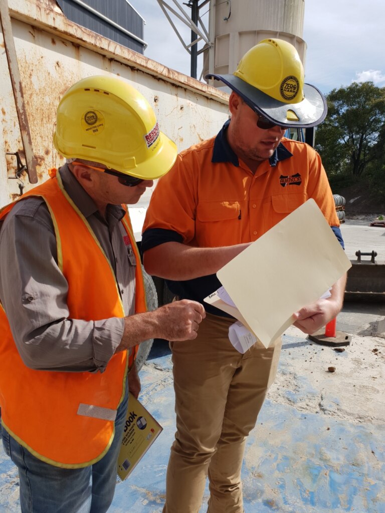 Two construction workers standing next to a sheet of paper.