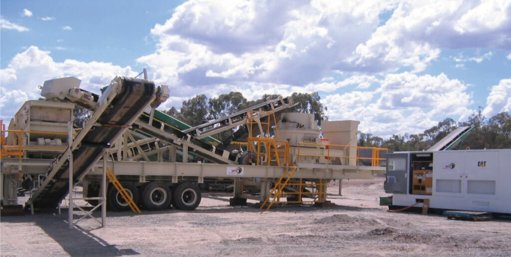 A mobile stone crusher in a field with a truck in front of it, ready to refurbish the Barmac Crushing and Screening Plant.