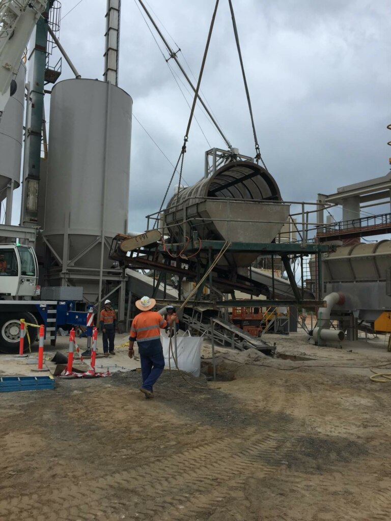 A crane is lifting a large container on a construction site using belt conveyors.