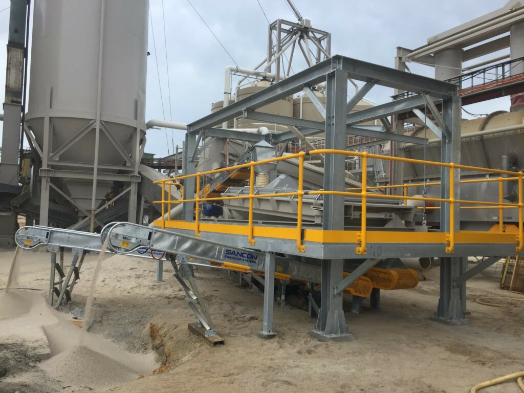 A truck loadout facility is equipped with a machine sitting on a conveyor belt in a factory.